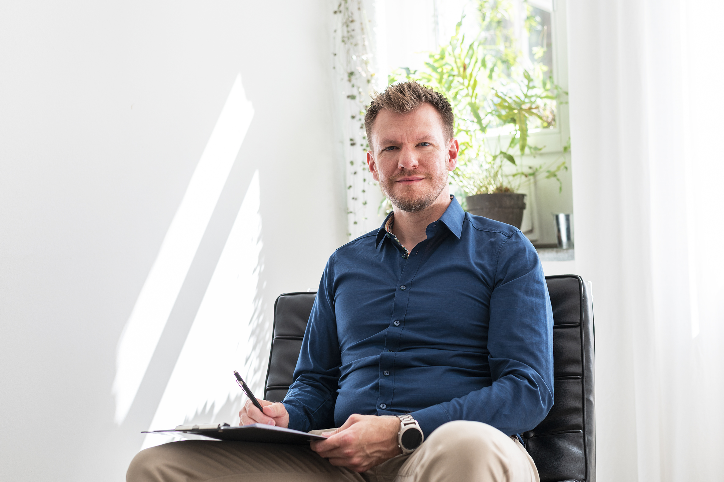 Dr. med. Krinninger in einem schwarzen Stuhl mit Klemmbrett und Stift