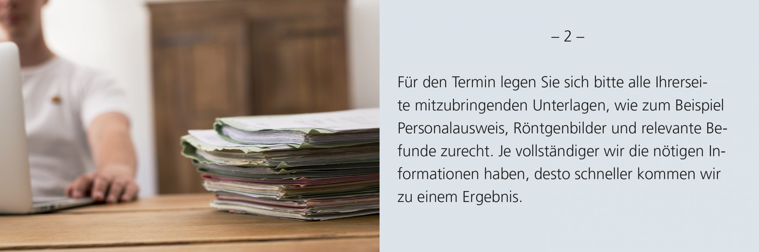 Aktenstabel auf einem Tisch. Im Hintergrund ist verschommen ein Mann an einem Laptop zu sehen